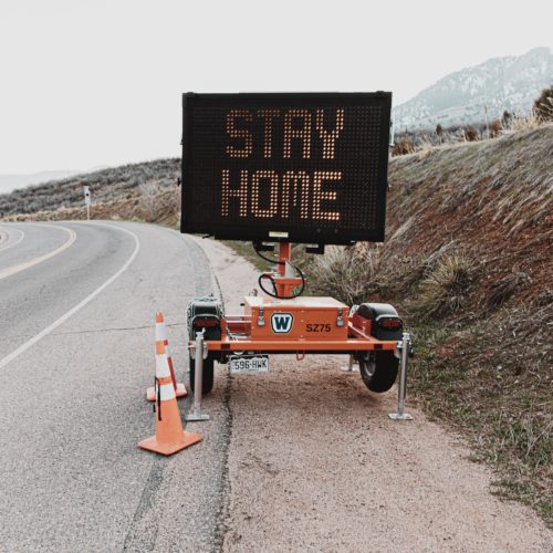 A digital sign says Stay Home on the side of an empty road. Road trip covid-19.